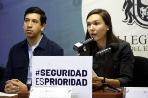 Susana de la Rosa hablando al micrófono en una conferencia de prensa. A su lado derecho se encuentra Pedro Kumamoto y frente a ambos un cartel con la leyenda “Seguridad es Prioridad”